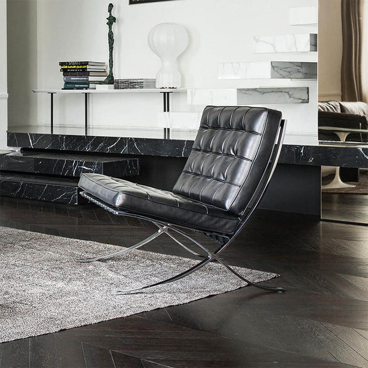 Barcelona chair replica in black leather, styled beside a marble staircase and sculpture